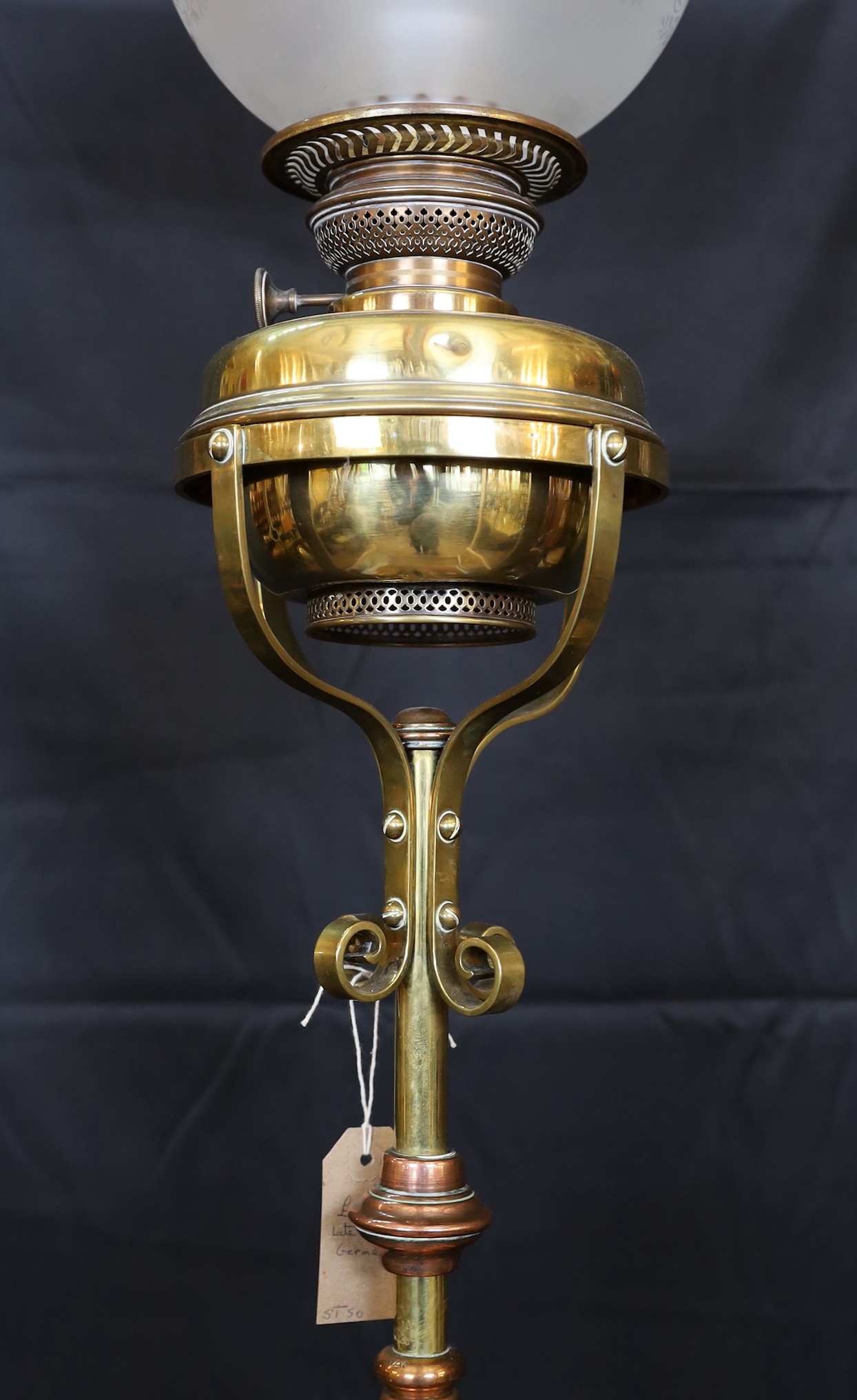 An Edwardian brass and copper telescopic oil lamp standard with scrolling underframe and etched glass globe, height 155cm. width 35cm